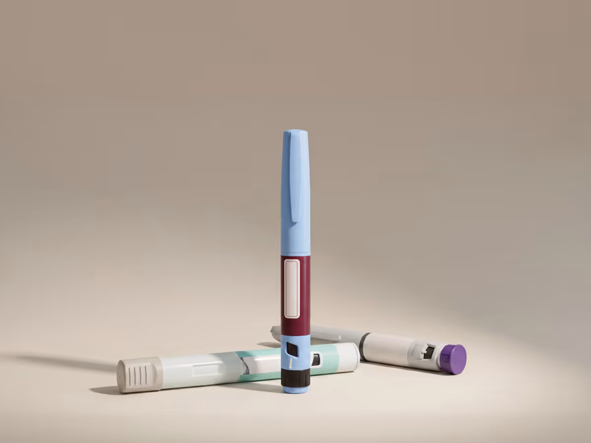 Three insulin pens on a beige surface, one standing blue and maroon, two lying horizontally.