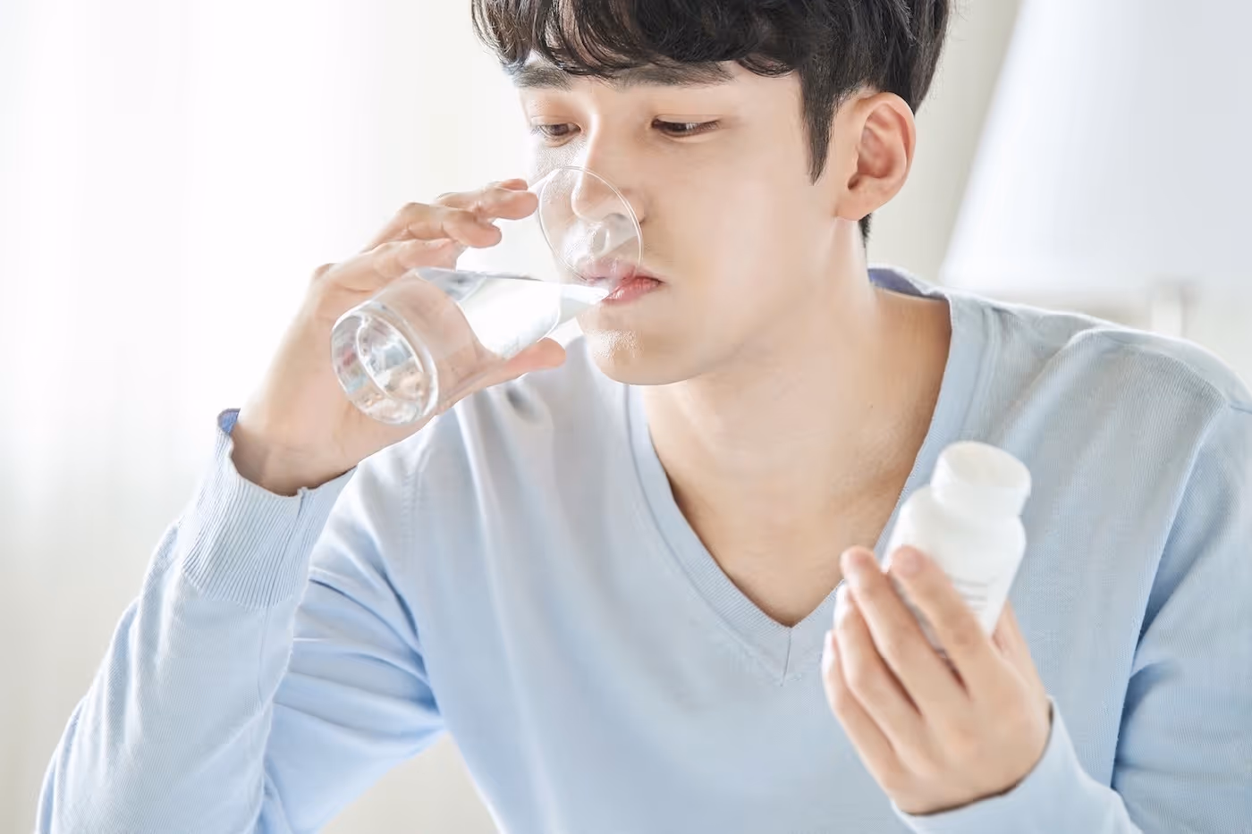 An Asian male drinking water to help swallow his medicines