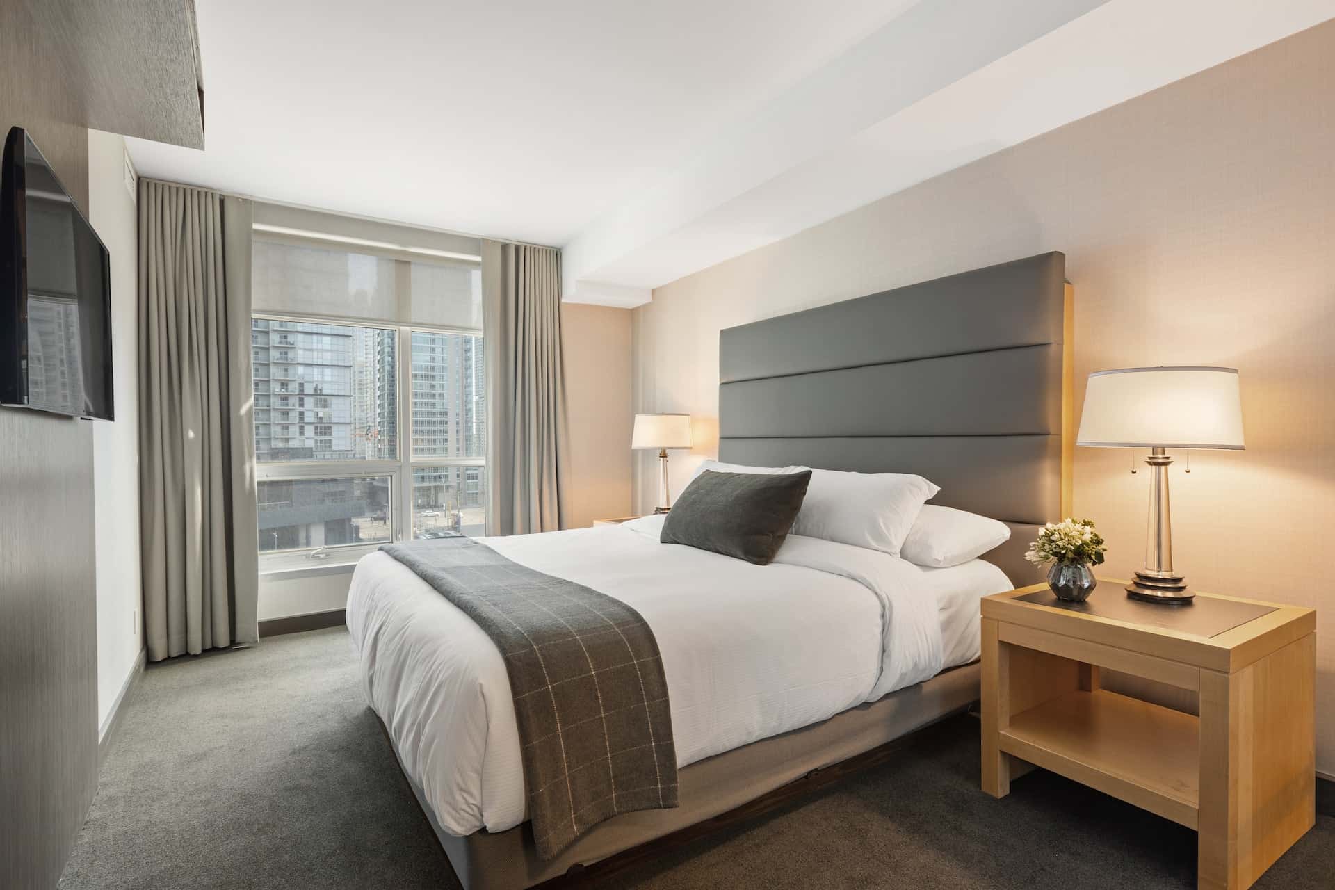 A hotel room with a queen-sized bed with a view of the surrounding high-rise buildings.