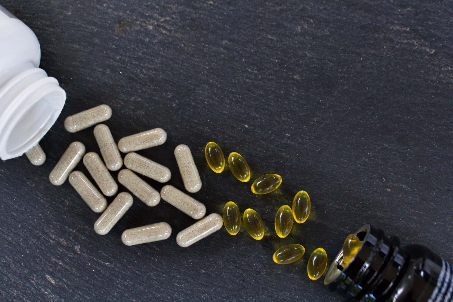 A white container beside a bunch of pills scattered on a table 