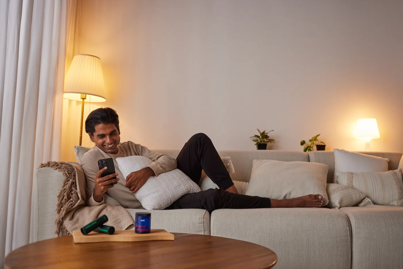 A man relaxing on a sofa with his phone under a warm lamp