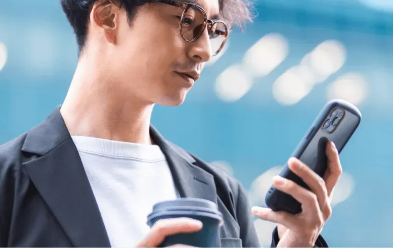 A young man holding a coffee and checking his phone
