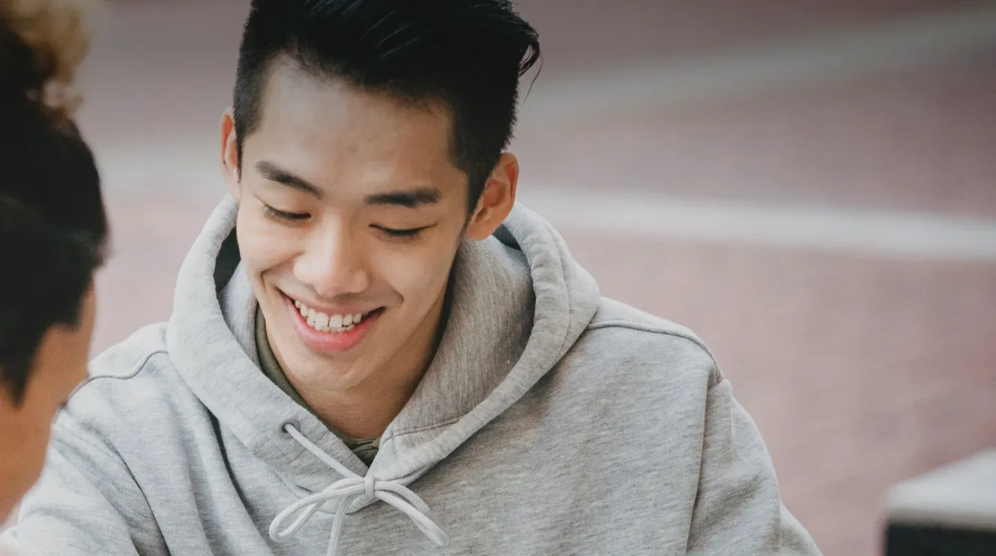 A young man in a hoodie smiling at his laptop