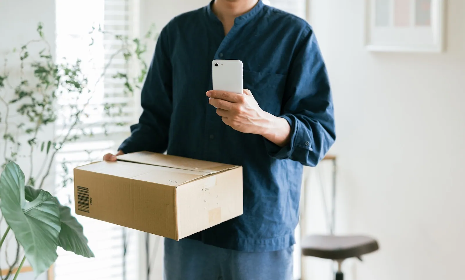 A man holding a parcel while simultaneously using his phone