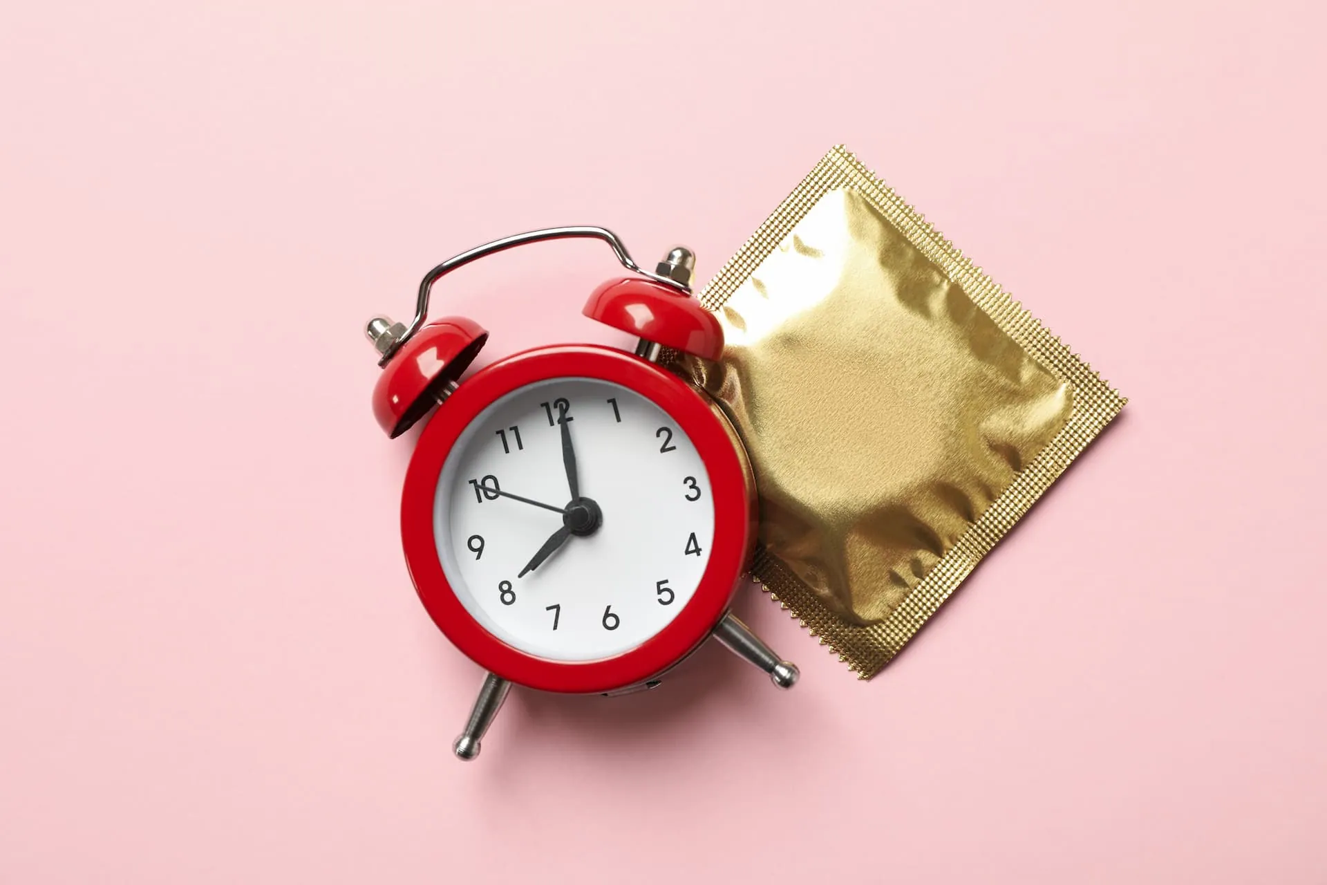 A red alarm clock next to an unopened condom