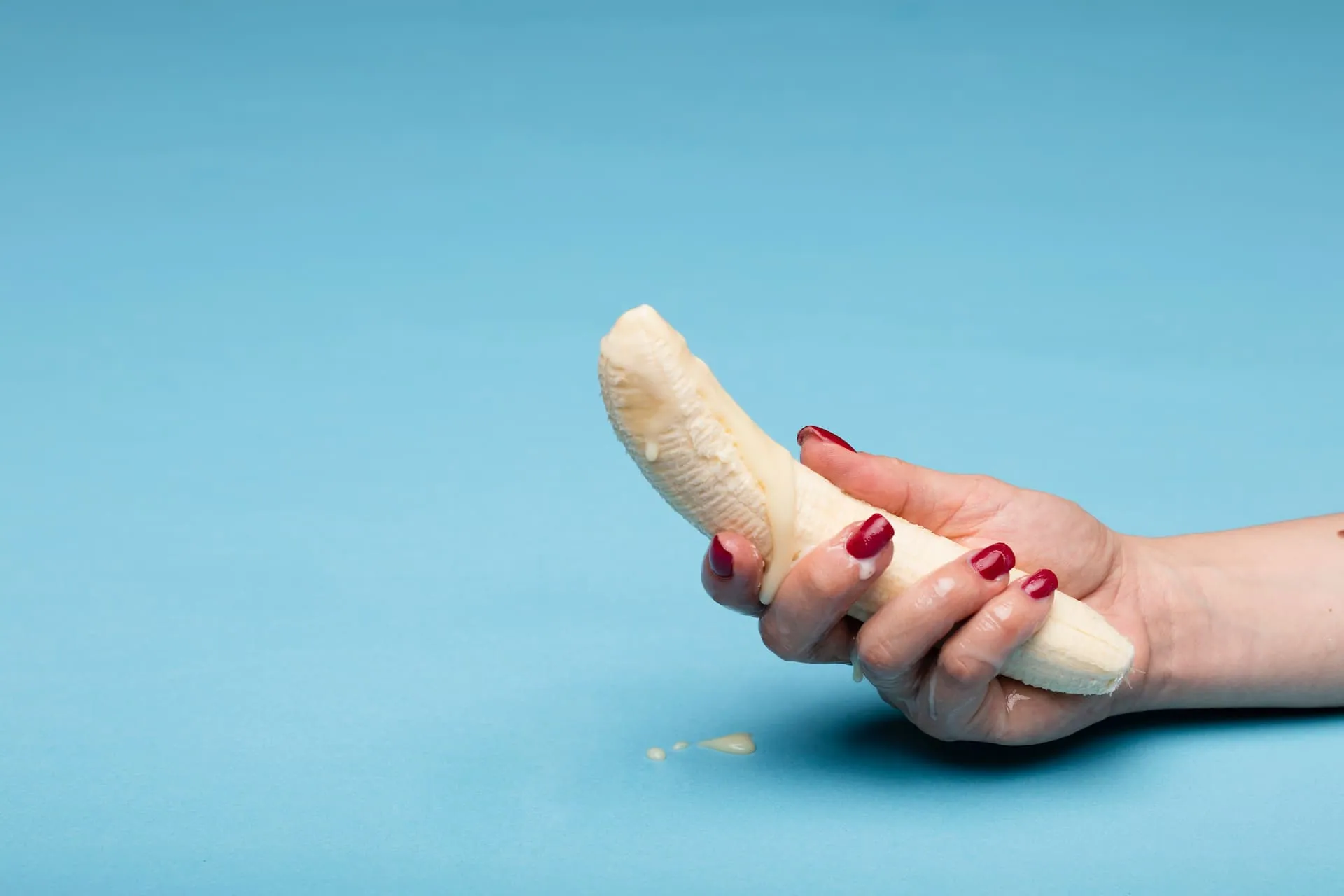 A woman holding onto a peeled banana with suggestive overflowing white tip. 