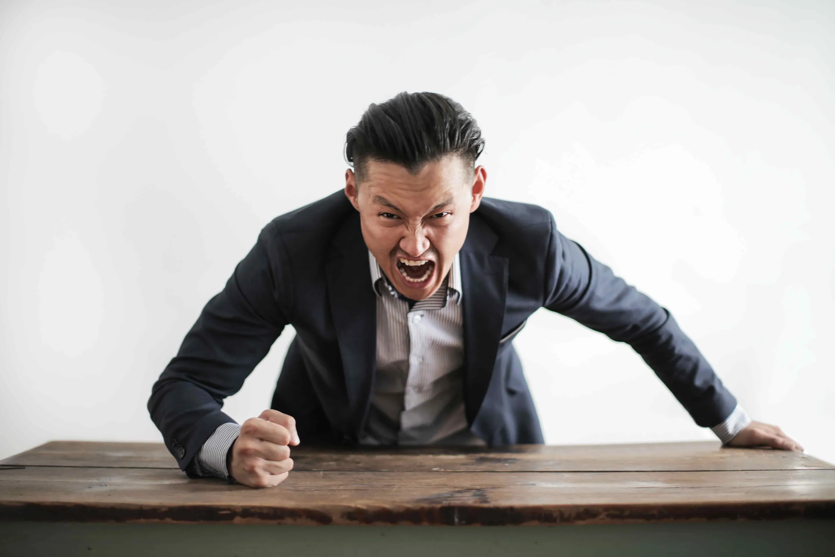 An angry Asian male with his fist clenched on a wooden table