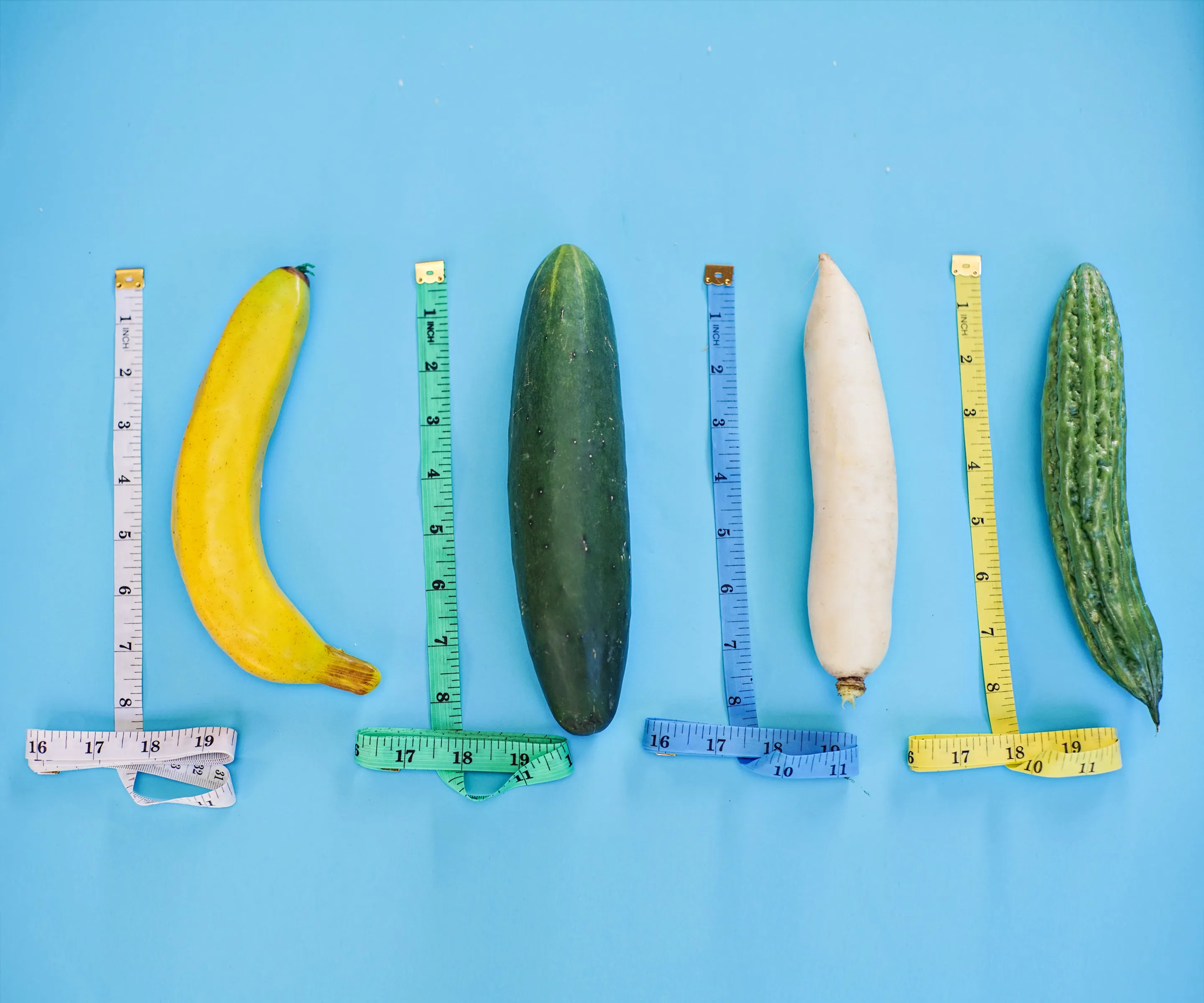 A banana, cucumber, radish, and okra being measured separately with measuring tape