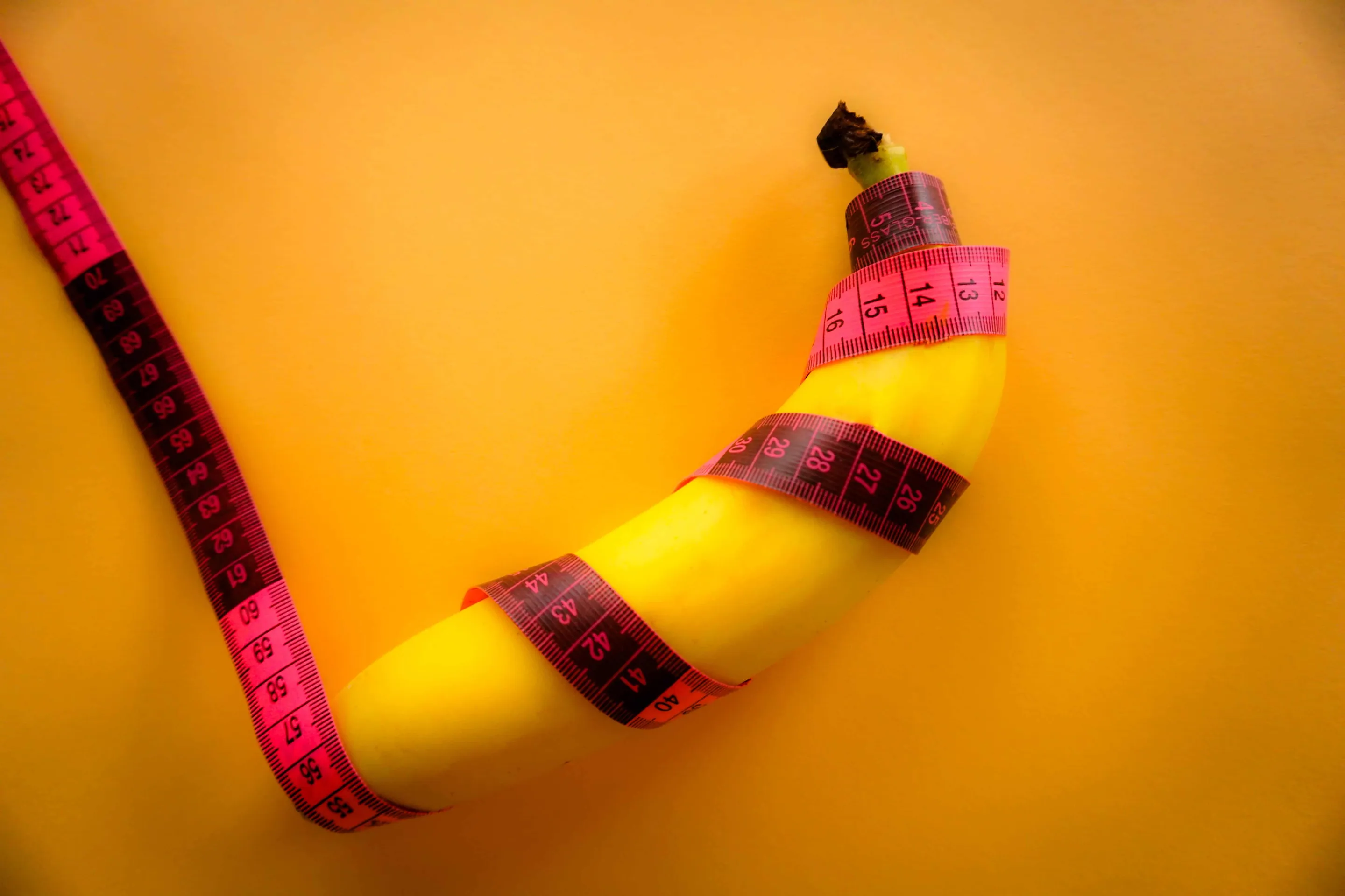A banana coiled in a blood red-coloured measuring tape