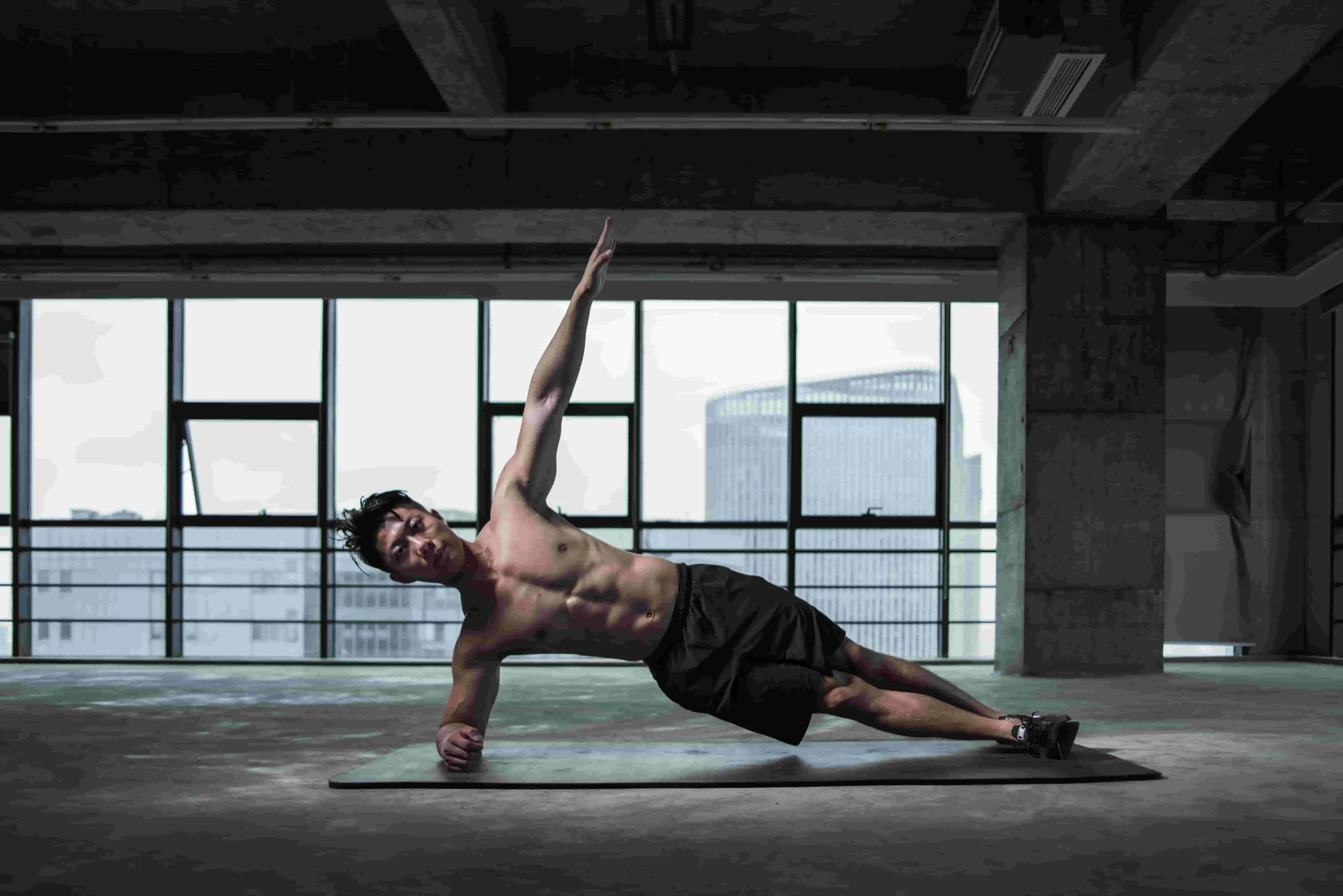 Lean and muscular Asian male doing side planks with his left arm raised towards the ceiling