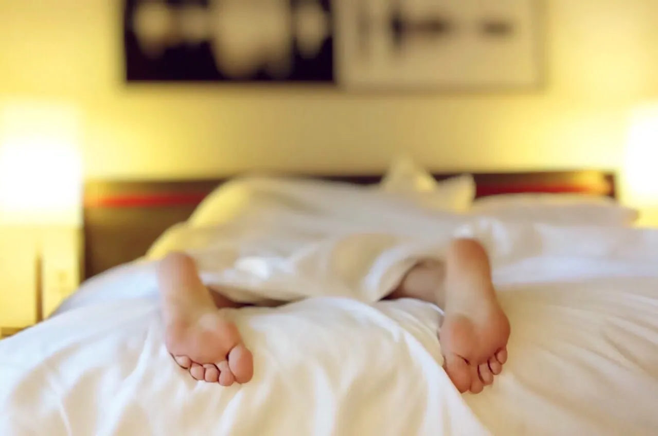 A person lying face down on on a bed, with a sheet covering their body. 