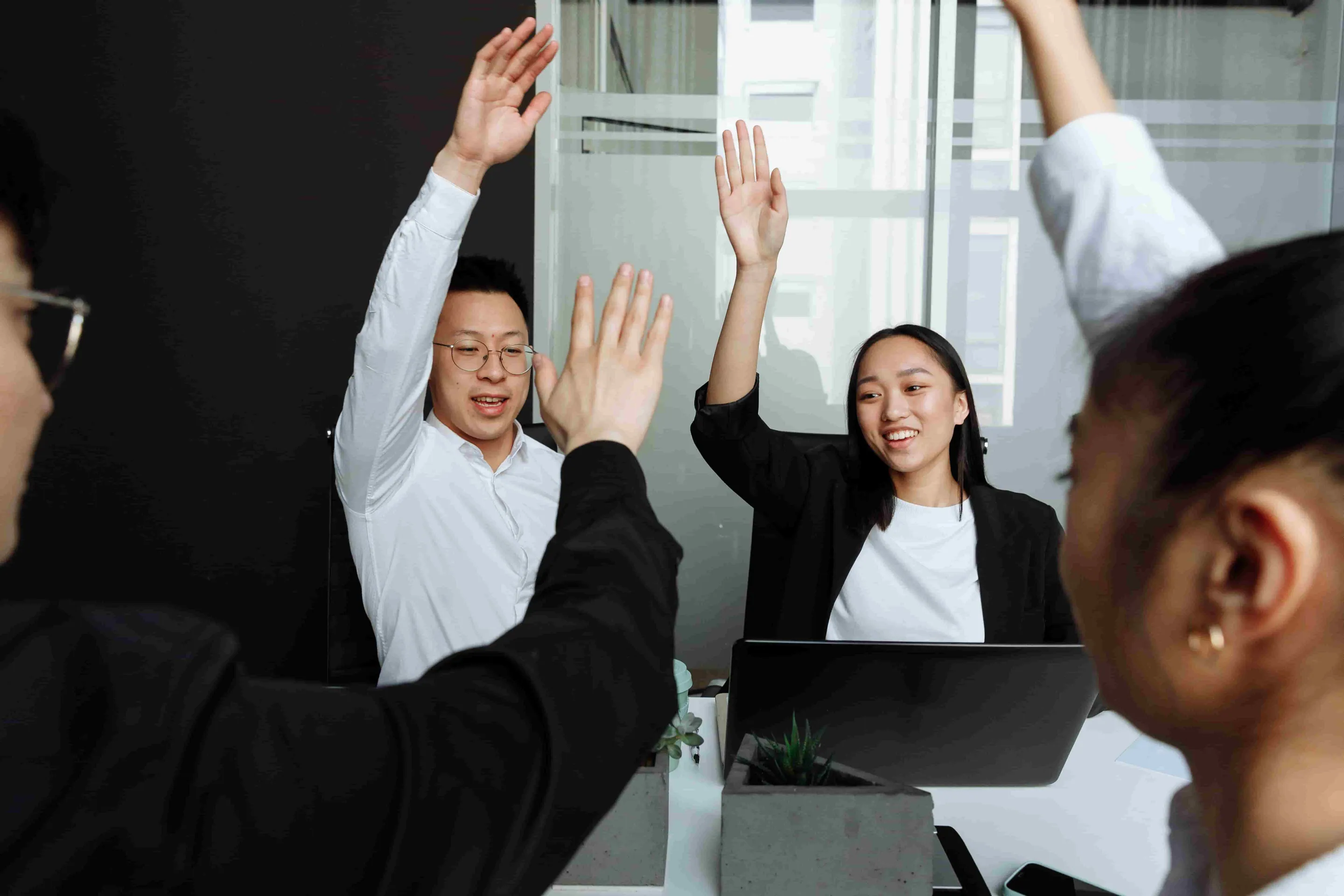 A group of Asian office workers enthusiastically raising their hands