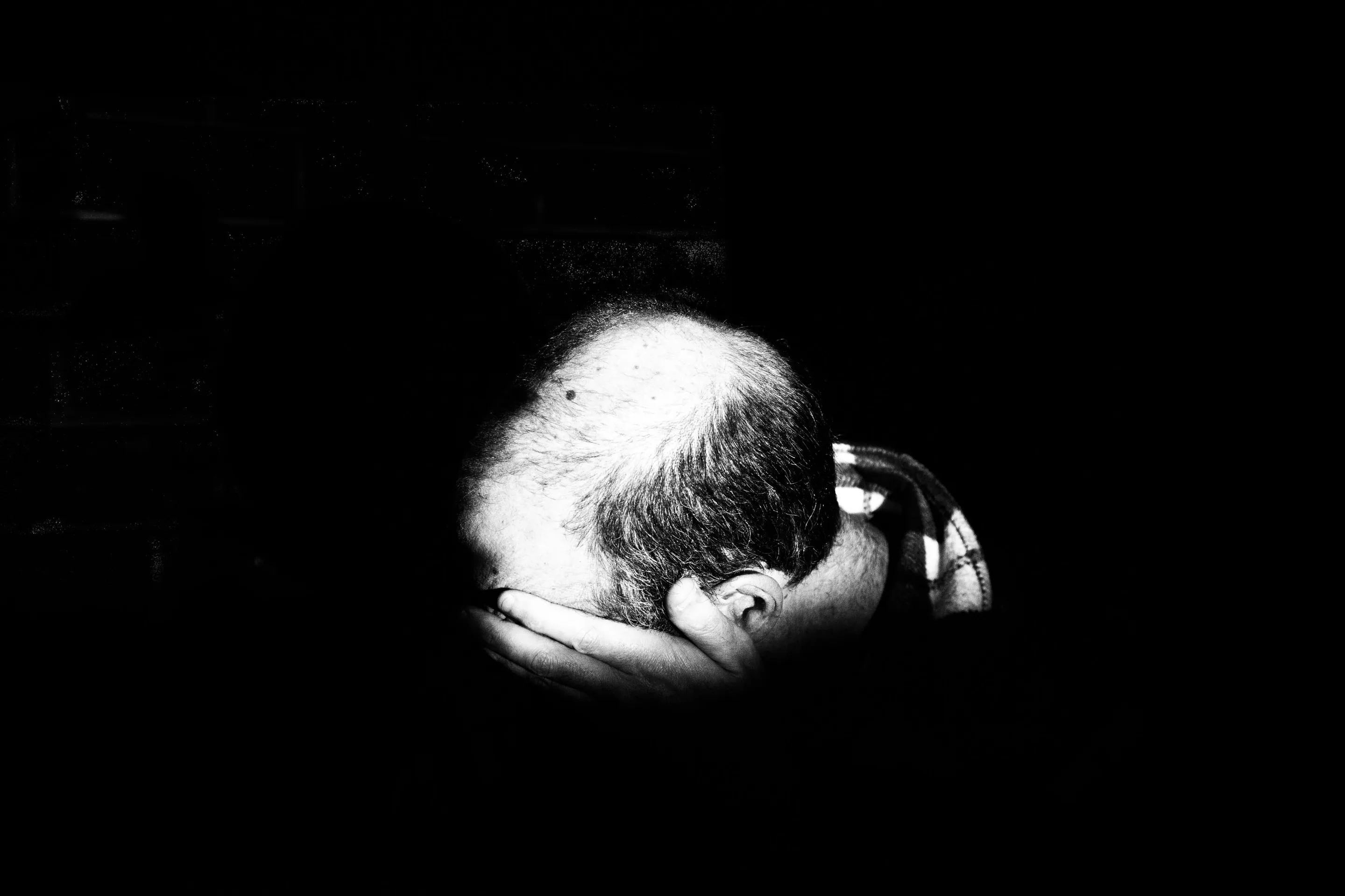 A black and white photo of a balding man covering his face